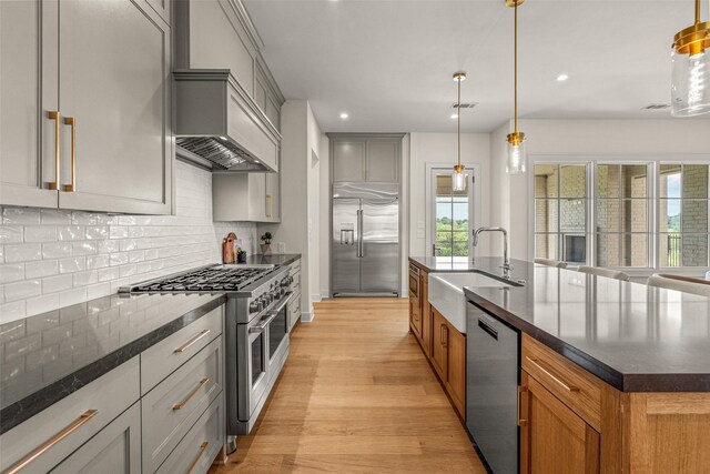 kitchen featuring gray cabinetry, sink, high quality appliances, light wood-type flooring, and dark stone countertops