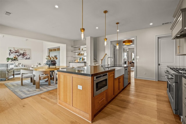 kitchen with sink, a kitchen island with sink, pendant lighting, stainless steel appliances, and light hardwood / wood-style floors