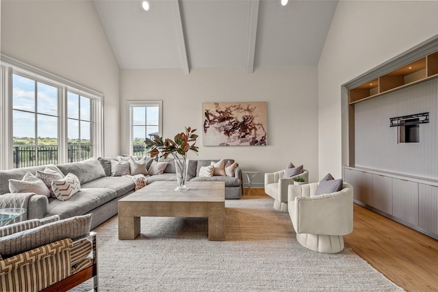 living room featuring beam ceiling, light hardwood / wood-style floors, and high vaulted ceiling