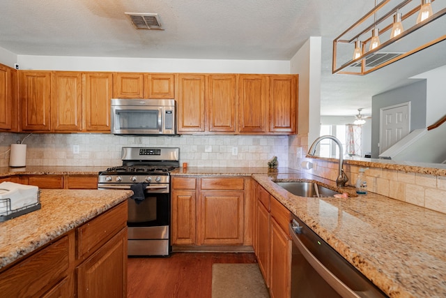 kitchen featuring wood-type flooring, stainless steel appliances, decorative backsplash, sink, and light stone counters