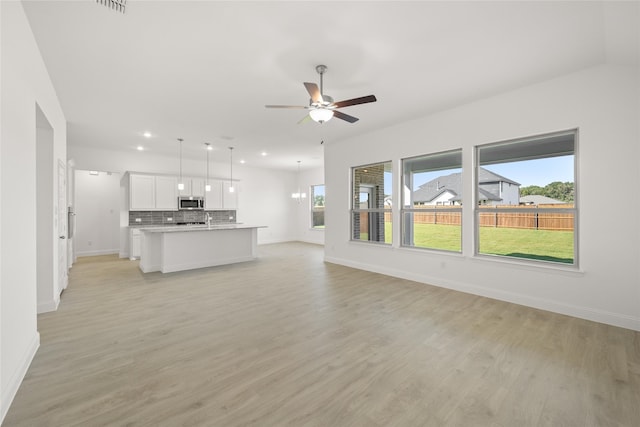 unfurnished living room featuring sink, ceiling fan with notable chandelier, and light hardwood / wood-style flooring