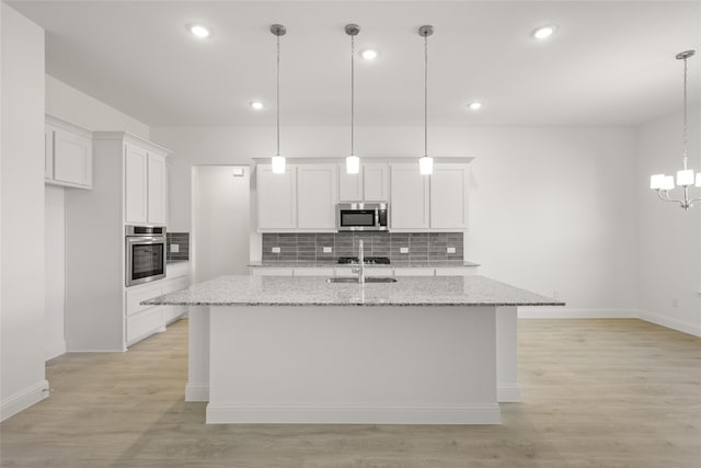 kitchen featuring light stone countertops, white cabinetry, appliances with stainless steel finishes, and a kitchen island with sink