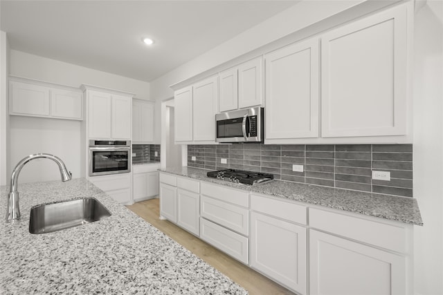 kitchen with sink, stainless steel appliances, white cabinets, and light stone countertops