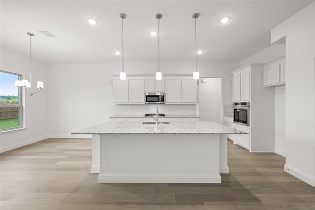 kitchen featuring light stone counters, white cabinetry, stainless steel appliances, and an island with sink