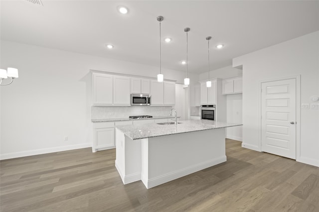 kitchen featuring white cabinets, stainless steel appliances, light stone counters, and a kitchen island with sink