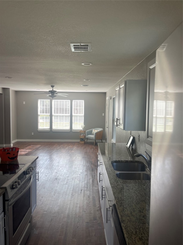 kitchen with dark wood-type flooring, stainless steel appliances, stone counters, ceiling fan, and sink