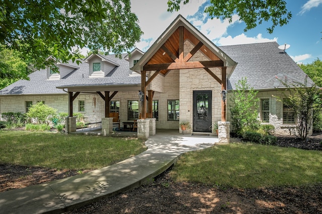 view of front of house featuring a shingled roof, a front yard, stone siding, and a patio