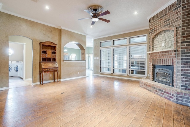 unfurnished living room with a brick fireplace, light hardwood / wood-style flooring, ornamental molding, ceiling fan, and washing machine and dryer