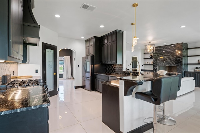 kitchen featuring tasteful backsplash, stainless steel refrigerator, light tile patterned floors, custom exhaust hood, and decorative light fixtures