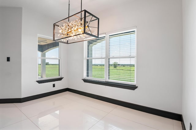 empty room with an inviting chandelier, a healthy amount of sunlight, and light tile patterned floors