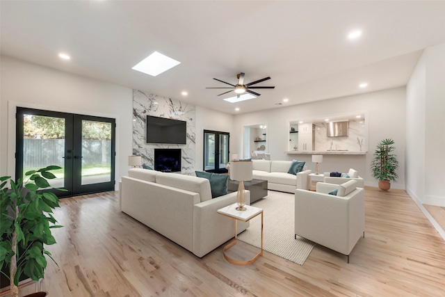 living room featuring a fireplace, french doors, a skylight, ceiling fan, and light wood-type flooring