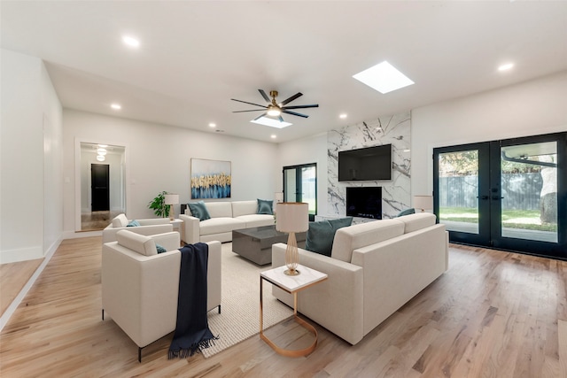 living room featuring light wood-type flooring, french doors, ceiling fan, and a premium fireplace