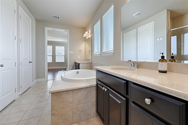 bathroom featuring a relaxing tiled tub, vanity, and tile patterned flooring