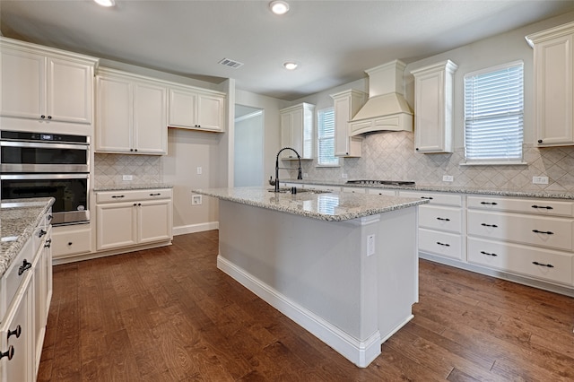 kitchen featuring custom exhaust hood, dark hardwood / wood-style flooring, an island with sink, sink, and appliances with stainless steel finishes