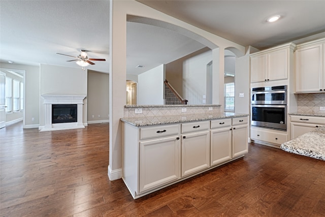 kitchen with decorative backsplash, dark hardwood / wood-style floors, light stone countertops, and double oven