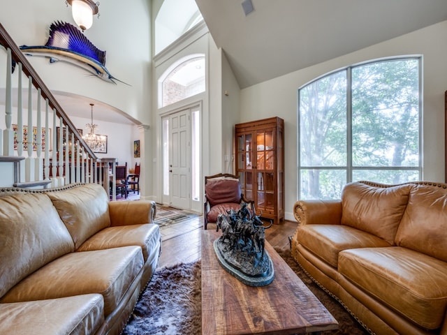 living room with a towering ceiling, wood-type flooring, a notable chandelier, and a wealth of natural light