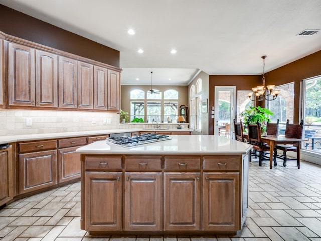 kitchen with pendant lighting, sink, tasteful backsplash, stainless steel gas cooktop, and an inviting chandelier