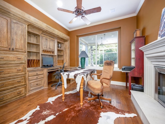 office area with ceiling fan, crown molding, hardwood / wood-style floors, and built in desk