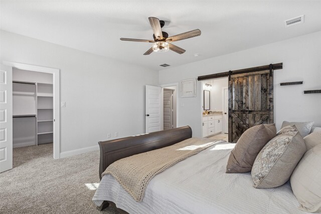 carpeted bedroom with a closet, a spacious closet, ceiling fan, a barn door, and ensuite bathroom