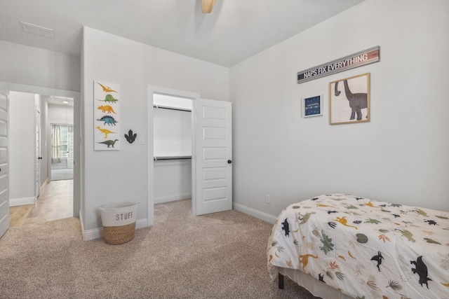 bedroom featuring a spacious closet, light carpet, a closet, and ceiling fan