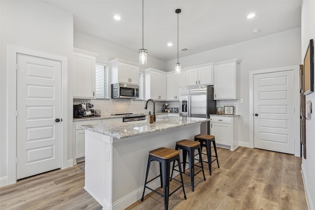 kitchen with appliances with stainless steel finishes, light hardwood / wood-style flooring, a center island with sink, decorative backsplash, and white cabinetry