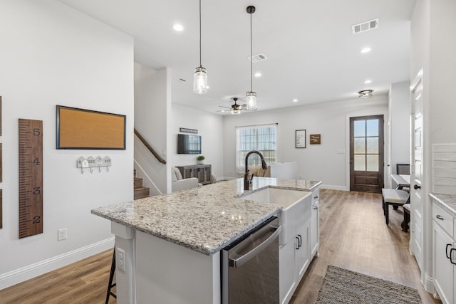 kitchen with stainless steel dishwasher, hanging light fixtures, an island with sink, sink, and light hardwood / wood-style floors