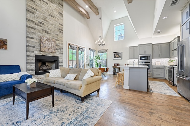 living room with a fireplace, an inviting chandelier, light hardwood / wood-style floors, beamed ceiling, and high vaulted ceiling