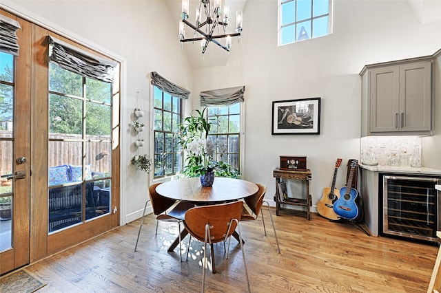 dining space featuring high vaulted ceiling, an inviting chandelier, wine cooler, and light hardwood / wood-style flooring