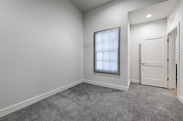 spare room with dark colored carpet, visible vents, and baseboards