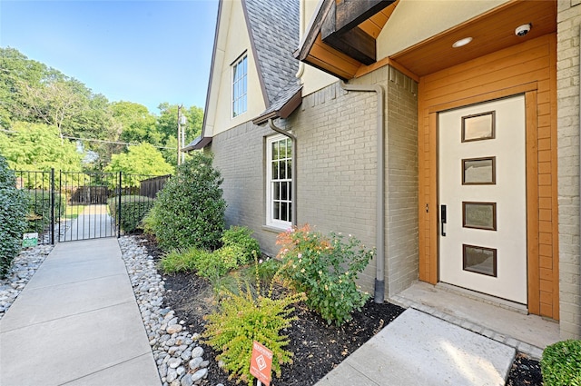 entrance to property with a shingled roof, a gate, fence, and brick siding