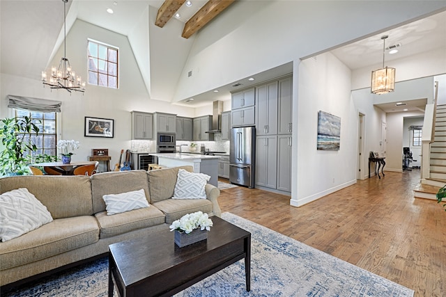 living room with beamed ceiling, high vaulted ceiling, a chandelier, and light hardwood / wood-style floors