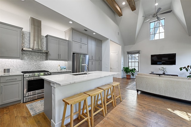 kitchen featuring dark hardwood / wood-style flooring, a breakfast bar, stainless steel appliances, high vaulted ceiling, and wall chimney range hood