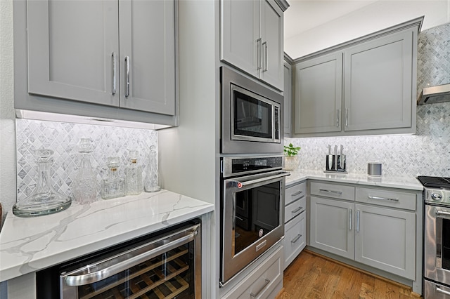 kitchen with tasteful backsplash, wine cooler, light stone countertops, appliances with stainless steel finishes, and light hardwood / wood-style floors