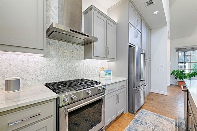 kitchen with gray cabinetry, high quality appliances, light stone counters, wall chimney range hood, and light wood-type flooring