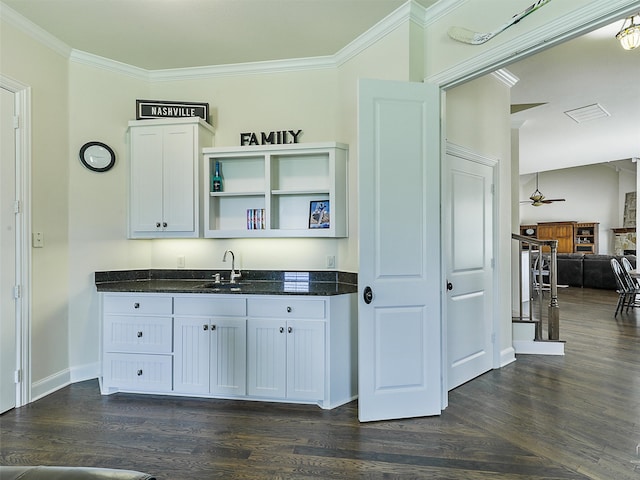 kitchen with dark wood-type flooring, dark stone countertops, a sink, and crown molding