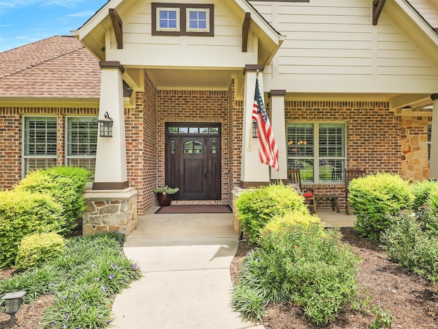 view of exterior entry with covered porch, brick siding, and a shingled roof