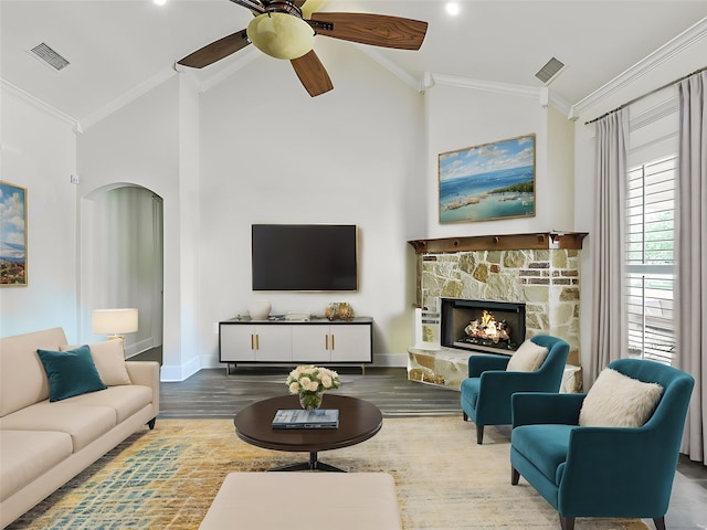 living room with a stone fireplace, high vaulted ceiling, hardwood / wood-style flooring, ornamental molding, and ceiling fan