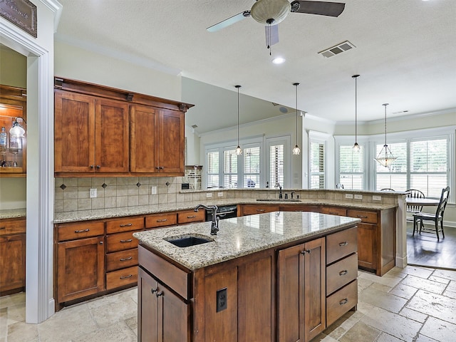 kitchen with pendant lighting, sink, light stone countertops, and a center island with sink