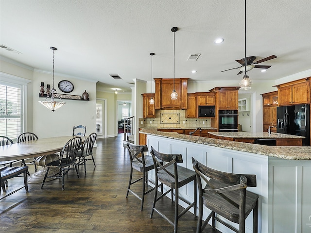 kitchen featuring backsplash, light stone countertops, black appliances, a kitchen bar, and decorative light fixtures