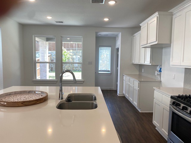 kitchen with stainless steel range with gas stovetop, decorative backsplash, white cabinets, sink, and dark hardwood / wood-style floors