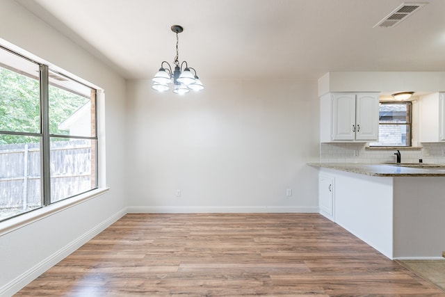 kitchen featuring light hardwood / wood-style flooring, white cabinets, an inviting chandelier, hanging light fixtures, and decorative backsplash