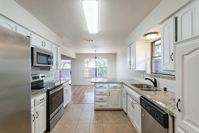 kitchen with white cabinetry, light tile patterned floors, kitchen peninsula, appliances with stainless steel finishes, and decorative backsplash