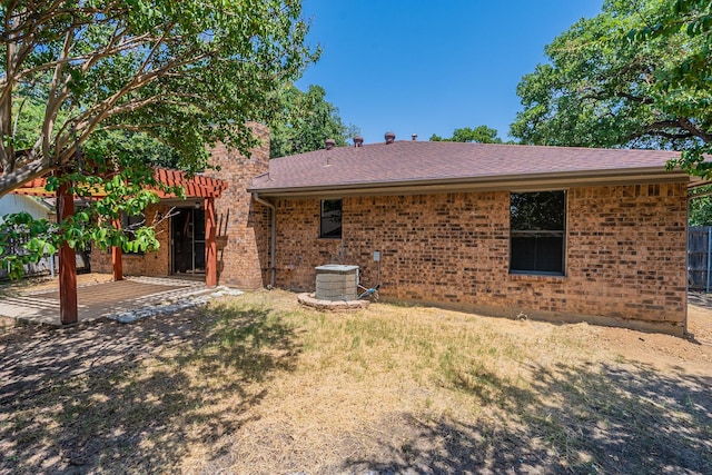 rear view of house with brick siding, a lawn, a shingled roof, and cooling unit