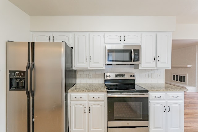 kitchen featuring appliances with stainless steel finishes, white cabinets, light stone counters, backsplash, and light hardwood / wood-style floors