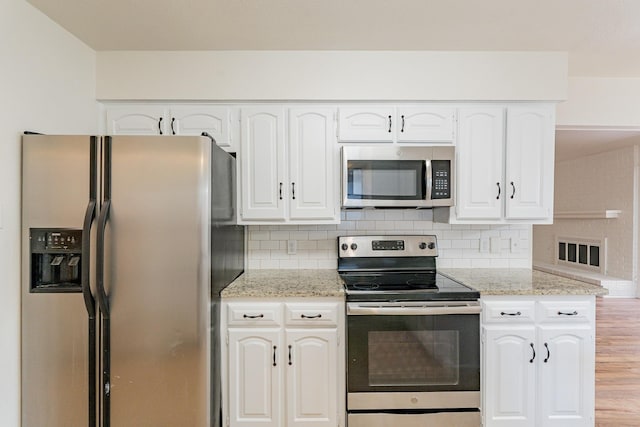 kitchen featuring appliances with stainless steel finishes, white cabinets, light stone counters, and tasteful backsplash