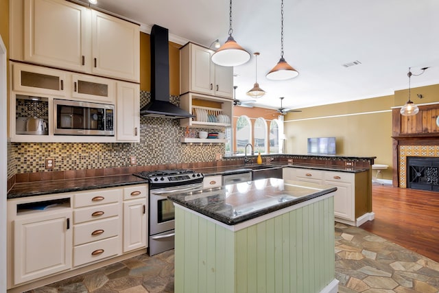 kitchen featuring a kitchen island, appliances with stainless steel finishes, a tiled fireplace, hanging light fixtures, and wall chimney exhaust hood