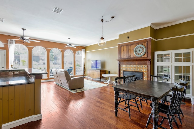 dining area with crown molding, hardwood / wood-style flooring, a tile fireplace, and ceiling fan