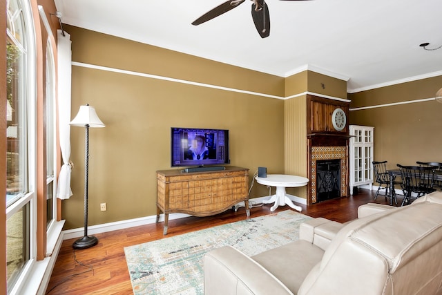 living room with ceiling fan, ornamental molding, wood-type flooring, and a fireplace