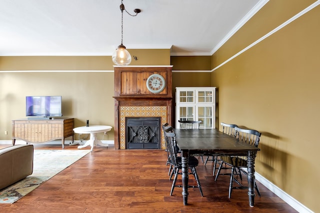 dining space featuring a tiled fireplace, ornamental molding, and hardwood / wood-style floors