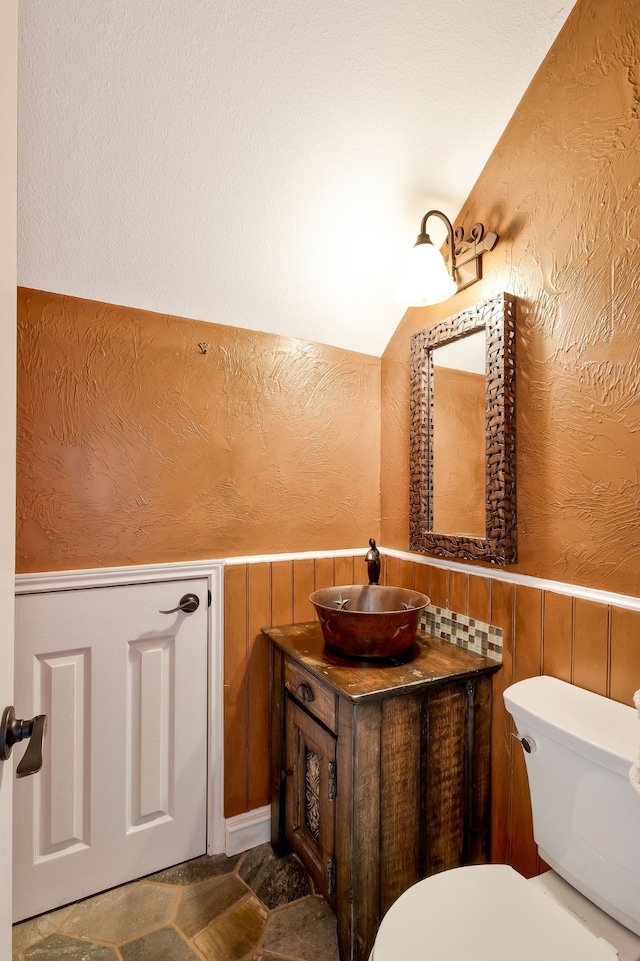 bathroom with wooden walls, lofted ceiling, toilet, and vanity